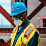 Construction worker in safety gear checking smartphone on a Detroit site.