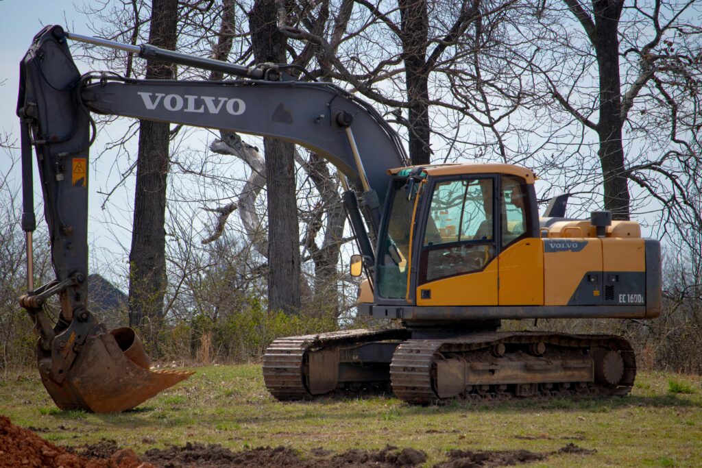 A Vovlo yellow excavator in a field with leafless trees, showcasing construction equipment in nature.