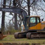 A Vovlo yellow excavator in a field with leafless trees, showcasing construction equipment in nature.