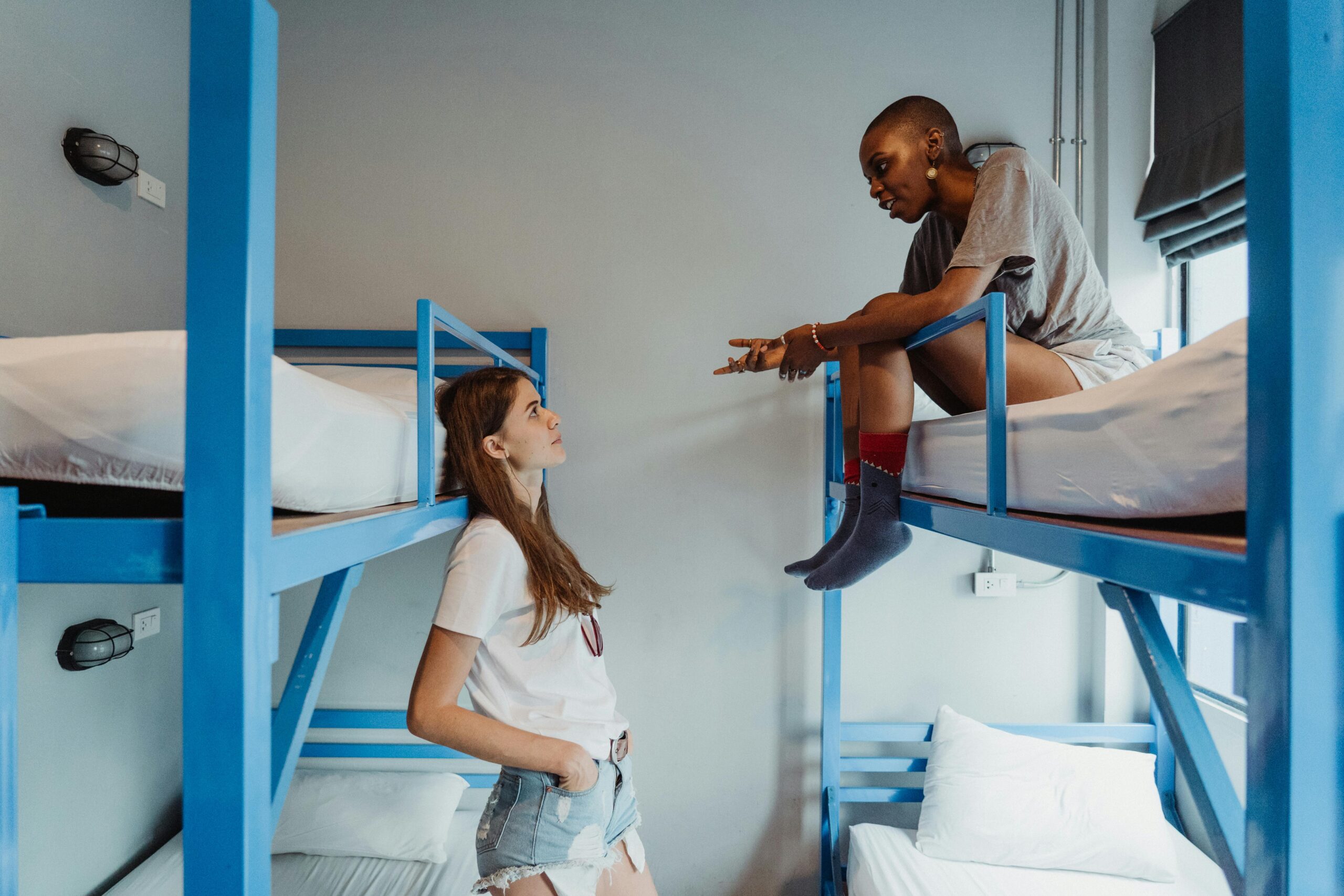 Two women engaging in conversation on bunk beds in a modern students hostel.