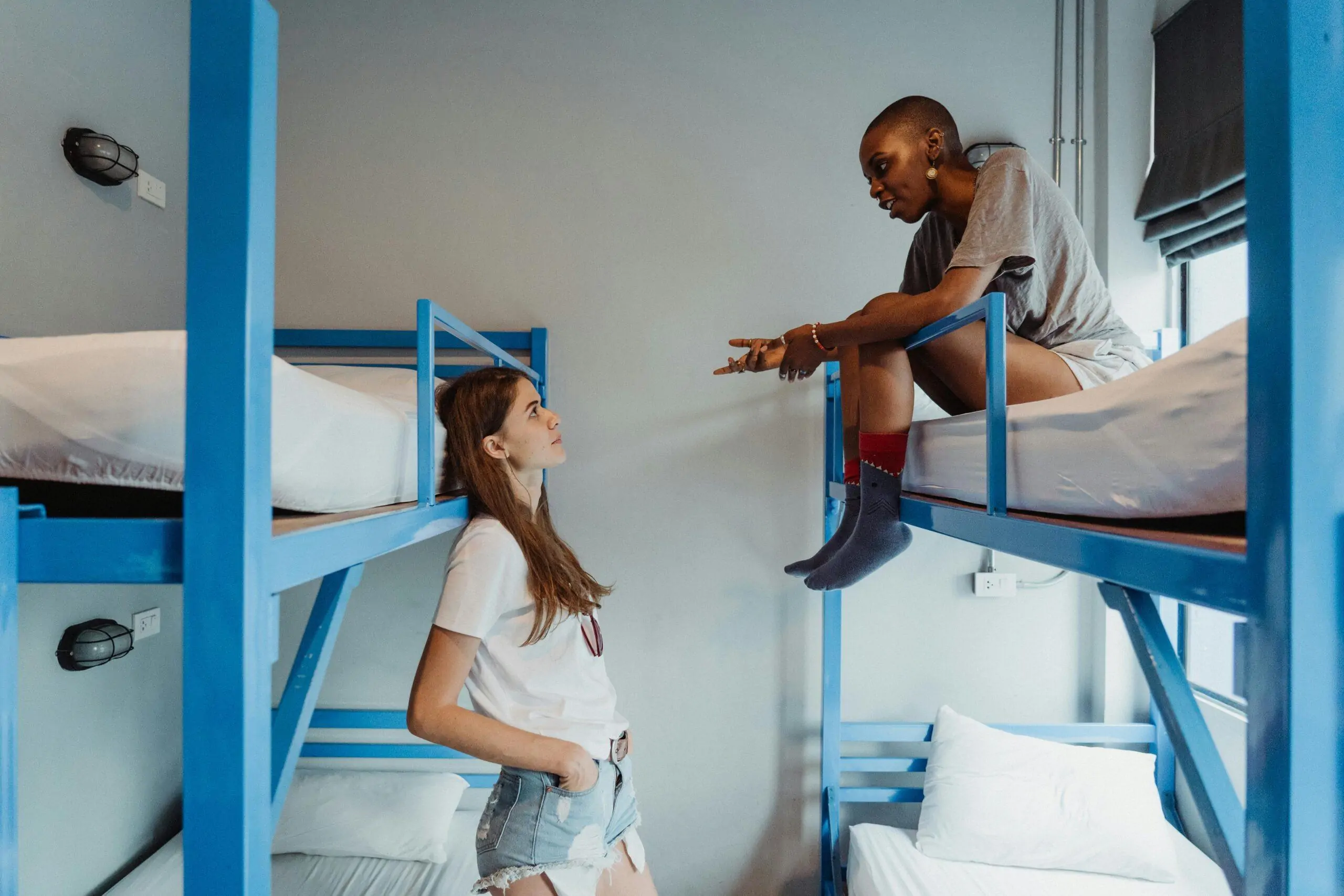 Two women engaging in conversation on bunk beds in a modern students hostel.