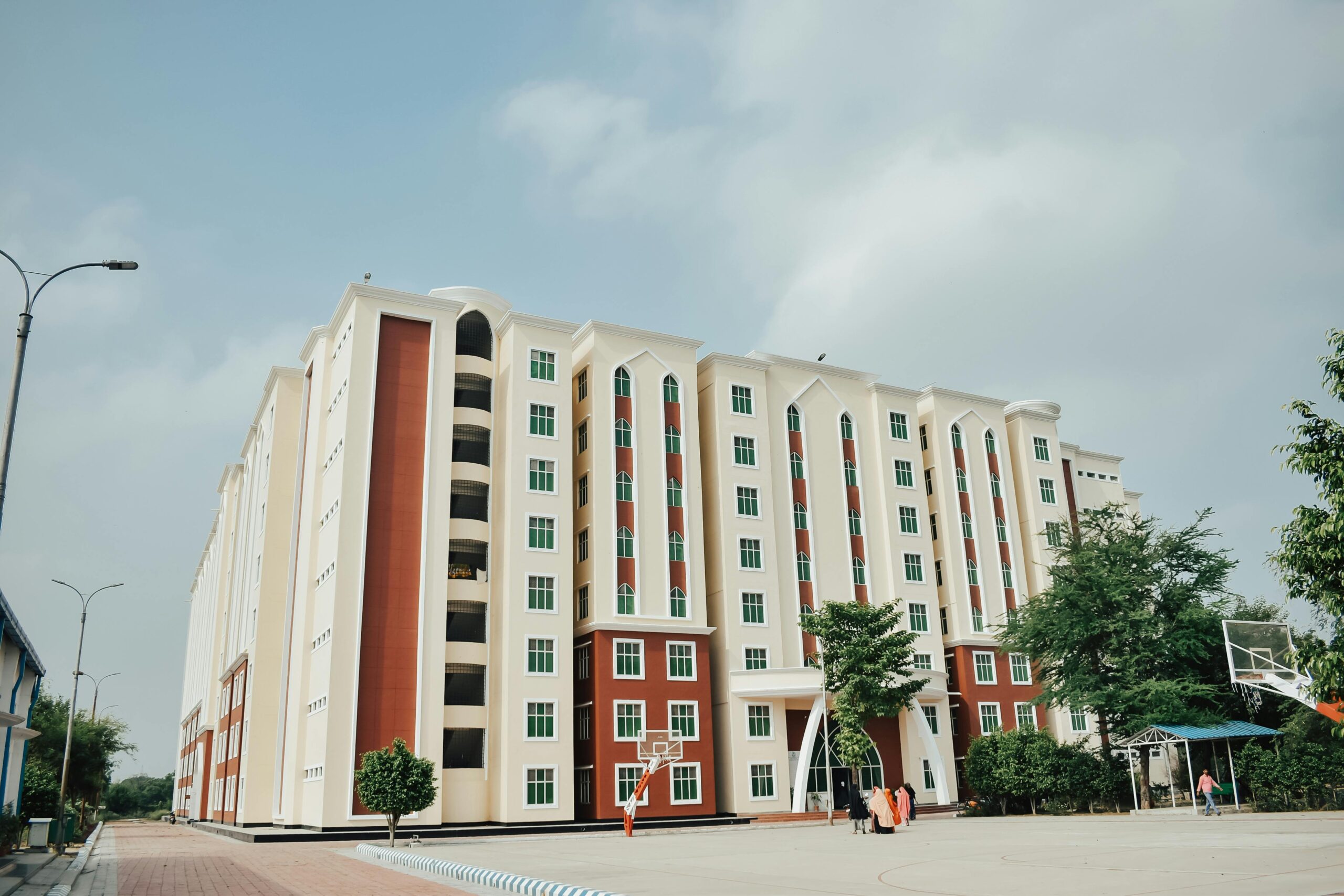 Spacious modern student hostel apartment building with a basketball court in a sunny urban setting.