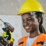 Confident female construction worker in safety gear smiling indoors.