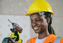 Confident female construction worker in safety gear smiling indoors.