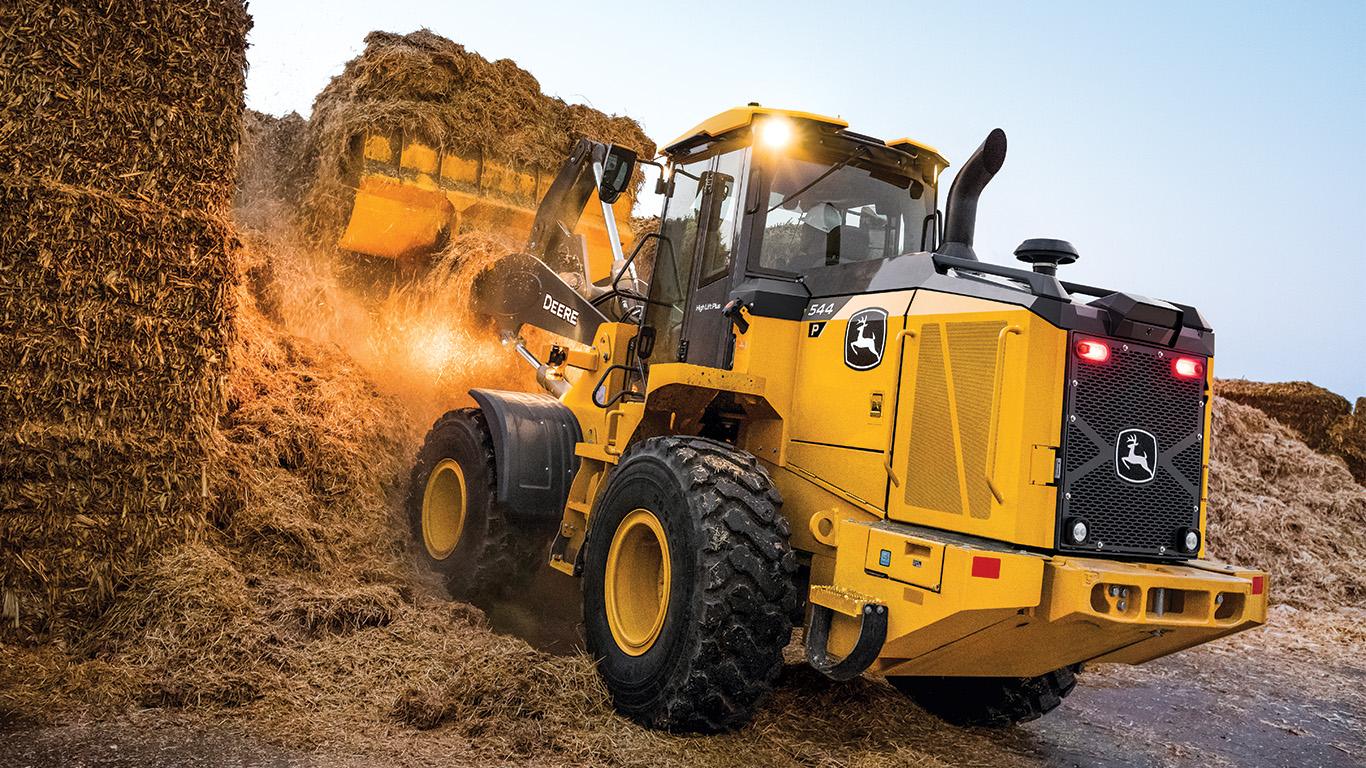 Yellow John Deere wheel loader moving hay bales